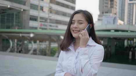 Young-smiling-business-asian-woman-using-smart-phone-on-the-city-street-while-talking-with-her-friend-on-the-mobile-phone-in-the-evening-of-Bangkok-Thailand.