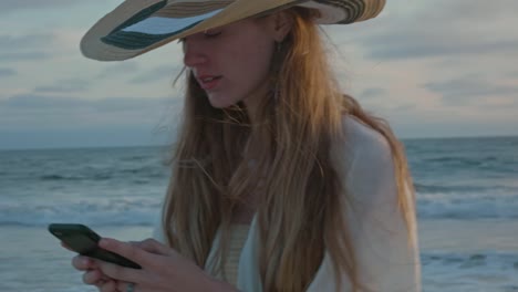 Young-woman-at-the-beach-texting-by-the-ocean-during-sunset