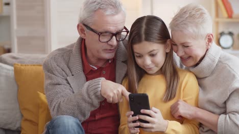 Abuelos-caucásicos-curiosos-viendo-a-la-nieta-usando-Smartphone