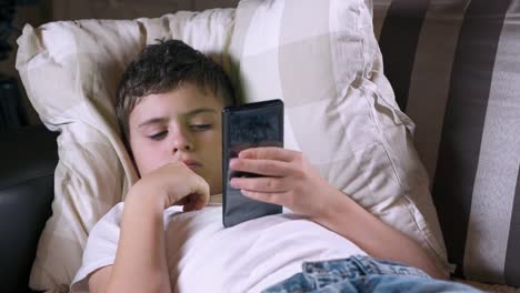 Teenager-boy-lies-on-a-sofa-and-plays-a-game-on-his-smartphone.-Social-media-and-child.-Cellphone-and-device-technology.-Phone-and-childhood.-Kid-and-telephone-in-life.-Cell-and-gadget.