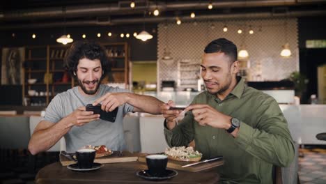 Young-afro-american-man-with-caucasian-friend-clicking-photo-with-smartphone-of-italian-bruschetta-with-coffee-in-cafe-while-enjoying-lunch-at-modern-cafe