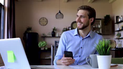 Hombre-de-negocios-feliz-sosteniendo-el-mensaje-de-mensajes-de-texto-del-teléfono-inteligente-en-la-oficina-en-casa,-recibiendo-mensajes-sms-leyendo-buenas-noticias,-utilizando-aplicaciones-móviles-útiles-para-los-negocios.