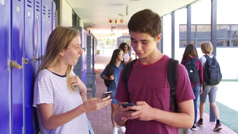 Dos-amigos-adolescentes-hablando-de-teléfonos-de-uso-en-pasillo-de-la-escuela