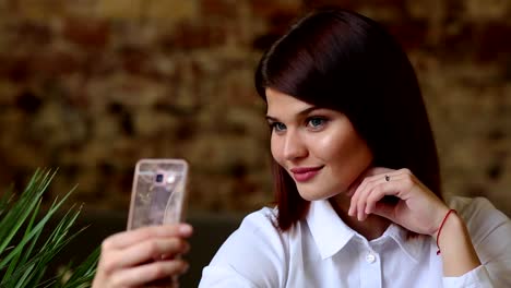 A-beautiful-girl-sits-in-a-cafe-and-after-drunk-a-hot-coffe,-poses-for-a-mobile-phone-camera-to-make-a-beautiful-self-for-social-networks