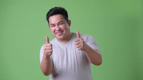 Young-handsome-overweight-Asian-man-against-green-background