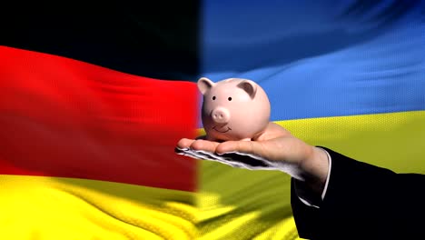 Germany-investment-in-Ukraine-hand-putting-money-in-piggybank-on-flag-background