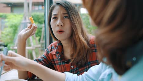 Beautiful-happy-Asian-women-lesbian-lgbt-couple-sitting-each-side-eating-a-plate-of-Italian-seafood-spaghetti-and-french-fries-at-restaurant-or-cafe-while-smiling-and-looking-at-food.