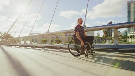 Young-happy-disabled-man-pushing-wheelchair-across-bridge-in-city-with-lens-flare