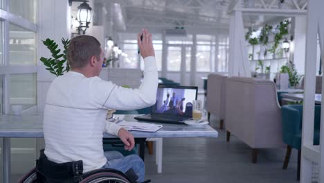 learner-handicapped-man-in-wheel-chair-writes-notes-in-notebook-while-watching-online-training-sitting-at-a-table-in-restaurant