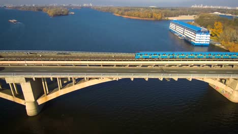 Aerial,-top-view-from-Drone:-Metro-train-travels-over-a-bridge-with-cars-and-trucks.