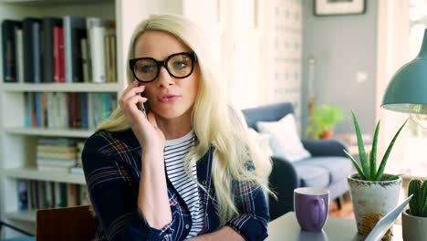 Attractive-Blond-Businesswoman-Talking-On-Smart-Phone-At-Home-Office