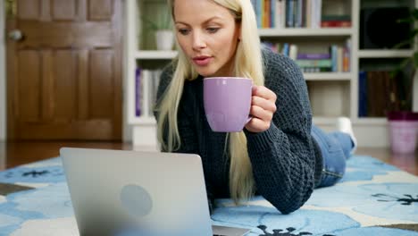 Hermosa-mujer-rubia-en-la-alfombra-usando-Laptop-tomando-té