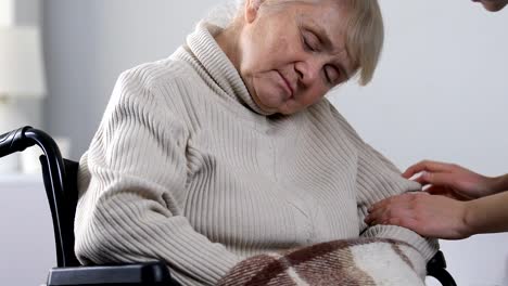 Nurse-taking-sleepy-aged-disabled-female-in-wheelchair-to-treatment-session