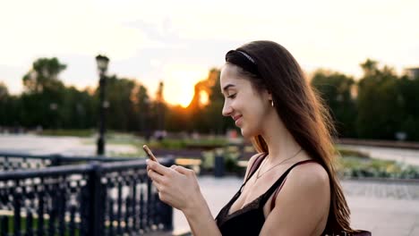 Hermosa-chica-modelo-mirada-teléfono-móvil-de-cierre-de-la-puesta-del-sol-y-teléfono-celular.-20S-mujer