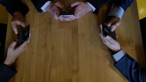 Top-handheld-shot-of-businesspeople-frantically-messaging,-typing,-chatting-on-their-smart-phone-screens,-camera-goes-up-and-they-look-at-camera-briefly-before-get-back-to-their-screens