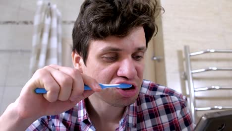 Young-man-cleans-his-teeth-and-looking-at-phone-in-the-bathroom.