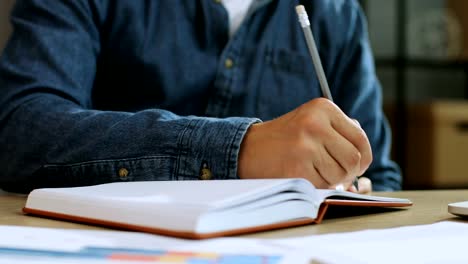 Close-up-shot-of-young-man-hands-making-noting-of-something-in-the-note-book-while-working-in-the-office.