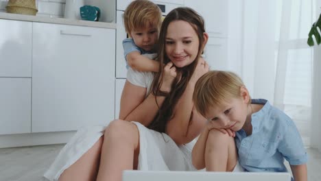 Mom-and-two-children-play-sitting-on-the-floor-hugging-and-having-fun.-A-happy-family.-The-game-after-viewing-the-laptop.-Games-with-children