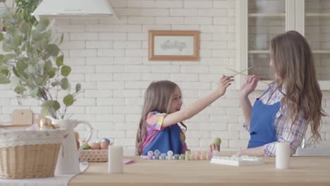 Niña-pequeña-pintando-huevos-con-su-madre-usando-un-cepillo-pequeño.