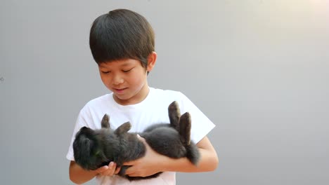 Joven-niño-Asiático-está-jugando-con-el-conejo-negro-encantador