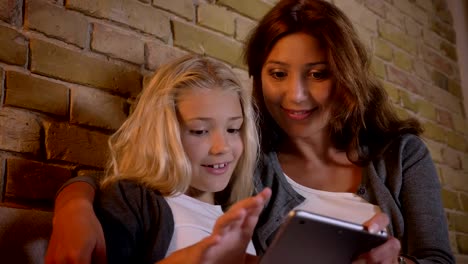 Closeup-shoot-of-young-caucasian-mother-and-her-pretty-small-daughter-using-the-tablet-and-getting-excited-sitting-on-the-couch-indoors-at-home