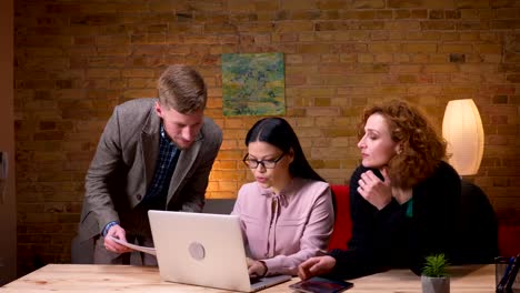 Closeup-Shooting-von-jungen-asiatischen-Geschäftsfrauen,-die-am-Laptop-arbeiten-und-mit-zwei-Kollegen-über-Daten-diskutieren.-Mitarbeiterinnen-mit-Tablet