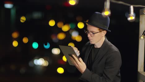 Hombre-joven-usando-la-tableta-en-la-azotea-en-la-ciudad-nocturna