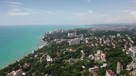 Luftvideos.-Panoramablick-aus-der-Höhe-der-Stadt-Sotschi.-Grüne-Bäume-und-Berge-am-Meer.-wohngebiet.-Hohe-Häuser-am-Strand.-Blauer-und-klarer-Himmel.