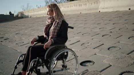 Mujer-alegre-usuario-de-silla-de-ruedas-está-sentada-en-el-terraplén-en-primavera-y-sonriendo