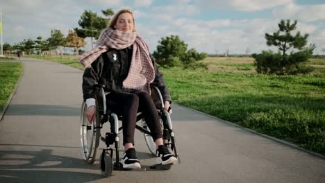 Woman-with-disease-of-legs-and-spine-is-riding-wheelchair-in-park,-smiling