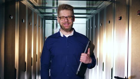 A-smiling-IT-specialist-is-standing-with-a-laptop-in-a-server-room