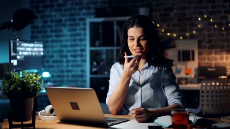 Chica-bonita-usando-el-teléfono-inteligente-que-graba-el-mensaje-de-voz-trabajando-en-la-oficina-por-la-noche