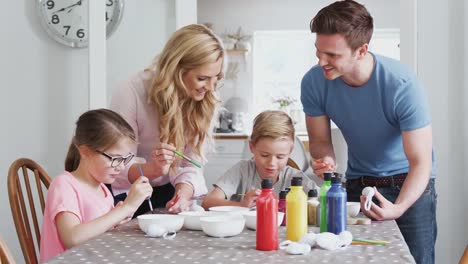 Familie-sitzt-um-Küchentisch-mit-Eltern,-die-Kindern-helfen,-Eier-für-Ostern-zu-malen---in-Zeitlupe-gedreht