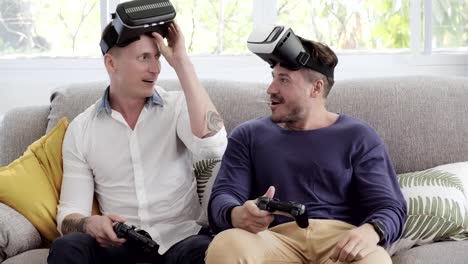 Pareja-gay-relajándose-en-el-sofá-jugando-juegos-de-realidad-virtual.-Emocionante-estado-de-ánimo.-Máscaras-fuera.