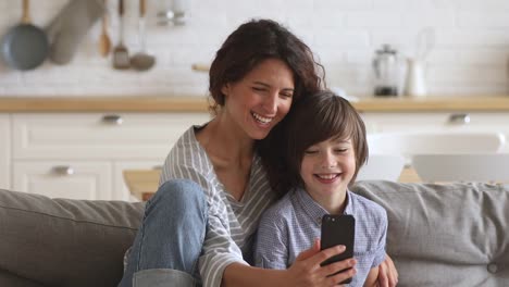 Feliz-madre-e-hijo-de-la-escuela-riendo-usando-el-teléfono-inteligente-en-casa