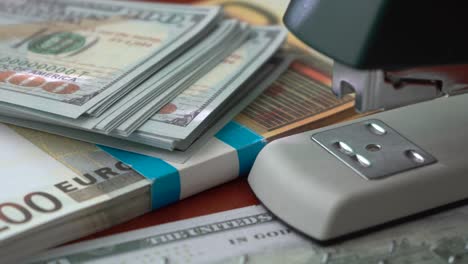 The-stapler-fastens-the-dollar-and-euro-notes-with-iron-clips.-Stapler-with-paper-clips-on-the-background-of-banknotes.-Counterfeit-money