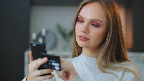 A-young-beautiful-woman-holds-a-smartphone-and-a-credit-card-while-paying-for-purchases-and-entering-a-pincode-to-pay-for-delivery.-Online-shopping