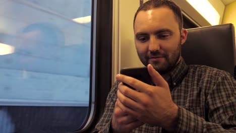 Hombre-guapo-sentado-en-un-tren-subterráneo-y-navegando-en-la-web-con-su-teléfono-inteligente