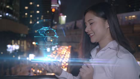 Junge-lächelnde-Business-asiatische-Frau-mit-Smartphone-interagieren-ein-Hologramm-Big-Data-3D-Erde,-Netzwerk-fortschrittliche-Technologie-der-Zukunft-auf-dem-Smartphone-Bildschirm.-Hintergrundstadt-Bangkok-Thailand.