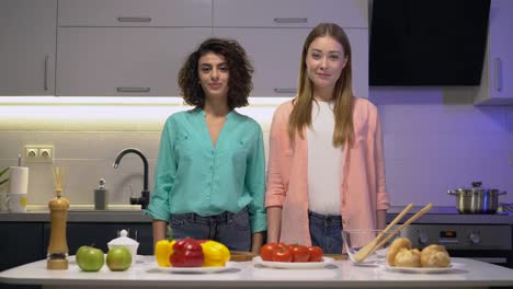 Dos-jóvenes-amigos-sonriendo-en-la-cámara,-mirándose,-cocinando-en-la-cocina