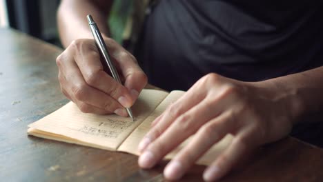 4K-Video-Kopie-Raum-des-Mannes-Hand-schreiben-in-weißen-Notizbuch-mit-Bokeh-Licht-im-Café-Hintergrund.