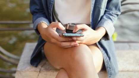 Close-up-of-asian-woman-using-smartphone-devices-sharing-social-media-while-sitting-beside-the-river-at-Bangkok-Thailand-on-vacation-summer.