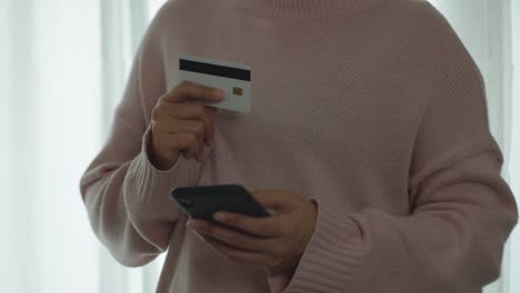 Nahaufnahme-Hand-der-asiatischen-Frau-hält-Smartphone-und-Kreditkarte-für-die-Zahlung-und-Online-Shopping-zu-Hause.-Glückliche-Frau-machen-Transaktion-mit-mobilen-Bank-Anwendung.-Online-Shopping-Konzept.