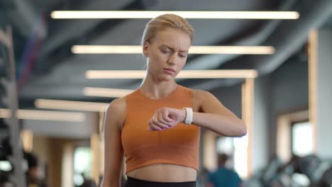 Upset-athlete-girl-using-smartwatch-at-gym.-Sportswoman-standing-in-sport-club