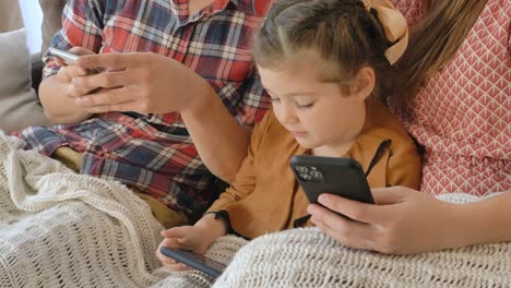 Kleines-Mädchen-mit-Eltern-spielt-in-Handys-sitzen-auf-dem-Sofa