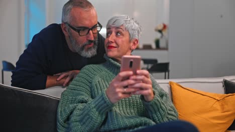 Seniorin-zeigt-Ehemann-Smartphone,-während-sie-auf-dem-Sofa-sitzt