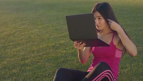 Young-woman-looking-in-laptop-as-in-in-mirror.-Asian-woman-sitting-on-grass