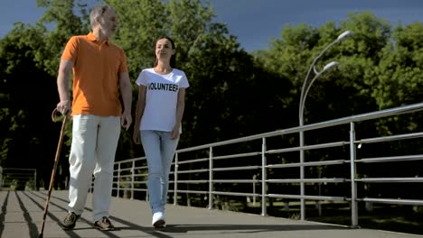 Delighted-senior-man-walking-with-a-cheerful-female-volunteer