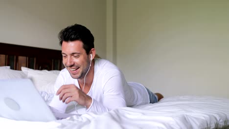 Young-Man-Using-Laptop-Computer-Having-Video-Chat-Call-Guy-Talking-Lying-On-Bed-In-Bedroom-Morning