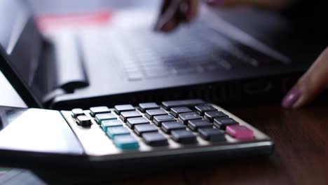 business-woman-hand-counting-on-calculator-with-blur-background-of-computer-laptop